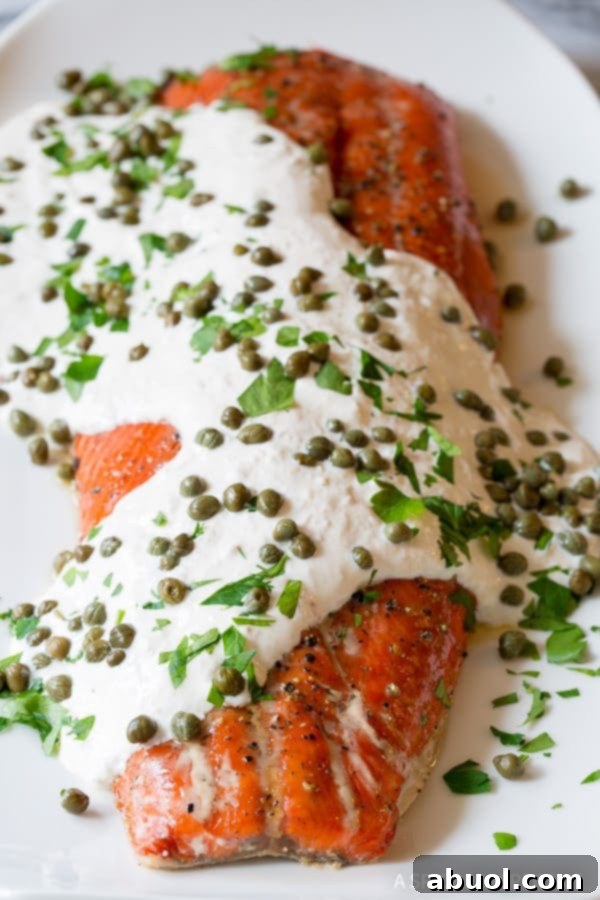 Smoky baked salmon with creamy white horseradish sauce on top, garnished with capers and fresh herbs.