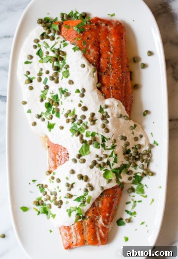 An overhead view of oven-baked salmon generously topped with creamy horseradish sauce and capers on a large serving platter.