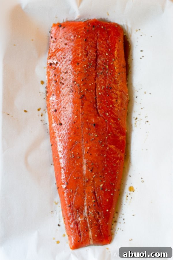 Raw salmon fillet generously seasoned with brown sugar and liquid smoke on a parchment-lined baking sheet.