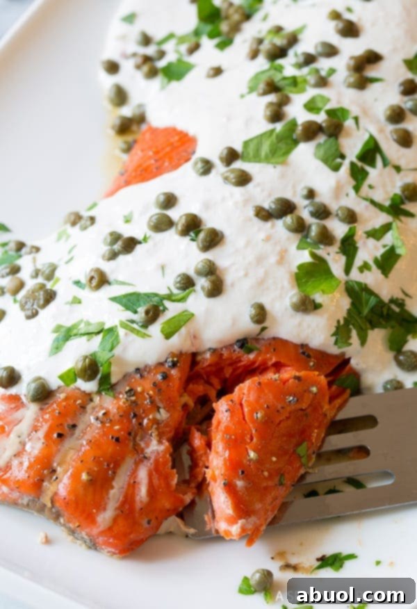 Close-up shot of baked salmon with horseradish sauce and capers, with a spatula gently flaking off a portion.