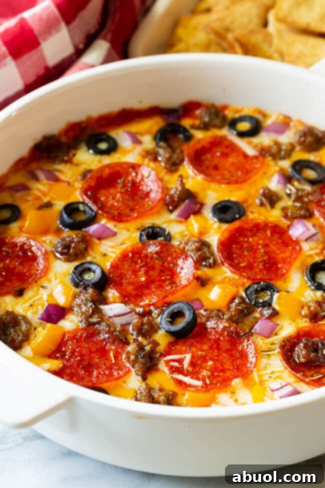A round white dish brimming with hot Supreme Pizza Dip, lavishly topped with crisp pepperoni slices, savory cooked ground sausage, delicate black olive slices, and finely chopped red onion.