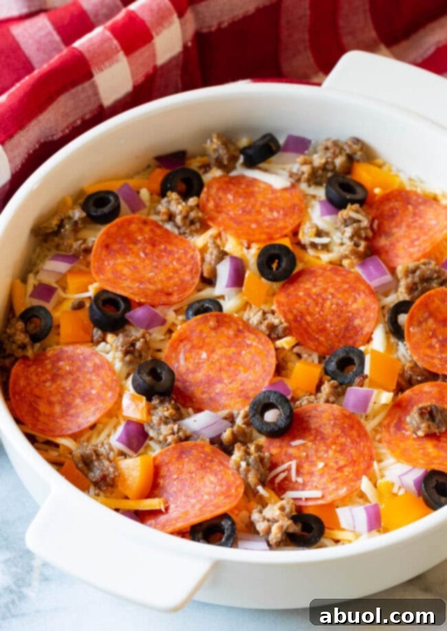 An overhead view of a white circular baking dish, freshly prepared with layers of cheese and pizza sauce, topped with vibrant uncooked pizza toppings including pepperoni, sausage, olives, bell pepper, and red onion, ready for the oven.
