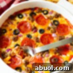 A round white dish with loaded supreme pizza dip, topped with pepperoni slices, ground cooked sausage, black olive slices, and chopped red onion.