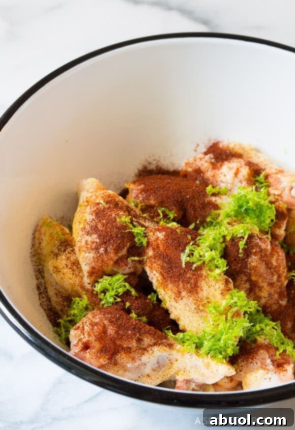 Chili Lime Wings Ingredients Chili Wings Recipe - Raw drummies and wingettes in a white bowl, plus fresh ingredients like spices and lime zest.