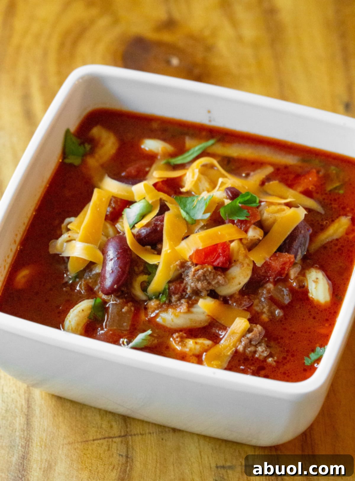 A close-up view of a single serving of slow cooker chili mac and cheese in a bowl, showcasing tender noodles, kidney beans, colorful vegetables, melted cheese, and fresh cilantro garnish.