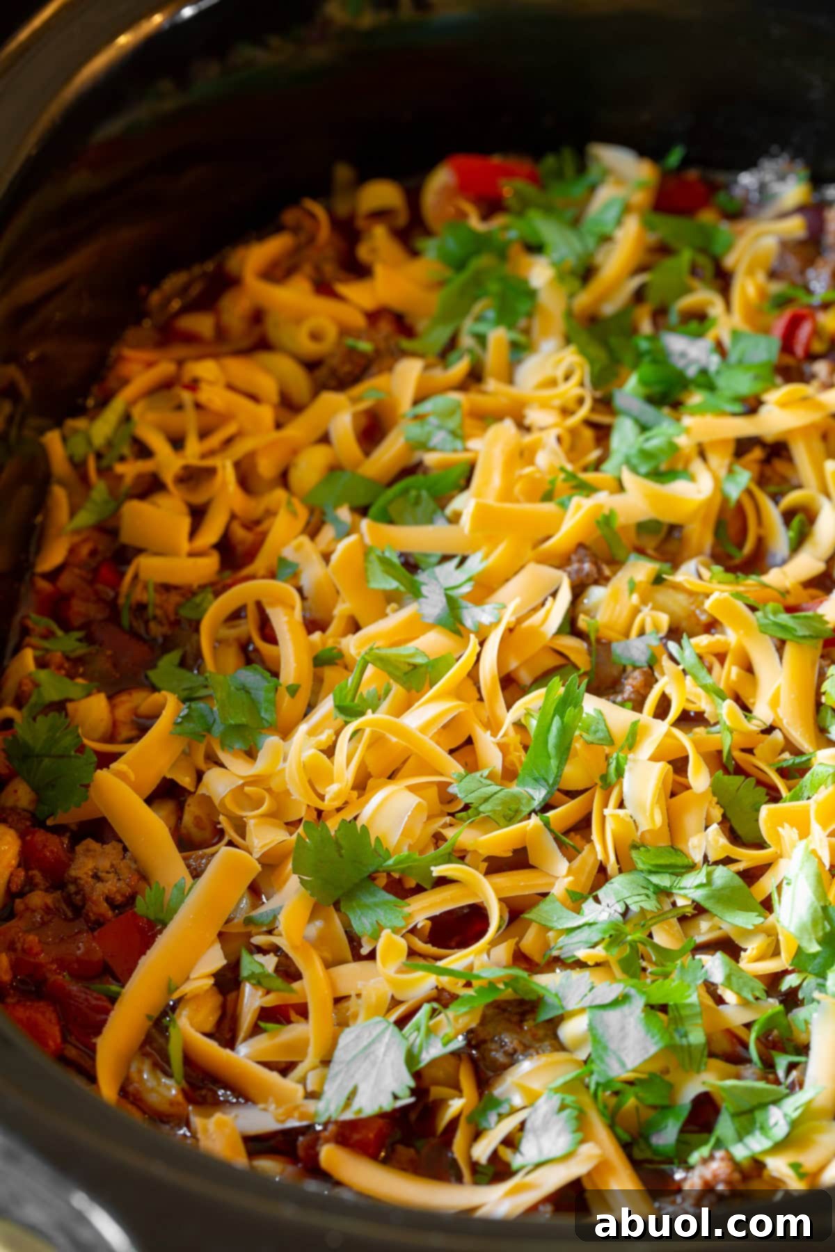 A generous topping of freshly shredded sharp cheddar cheese and vibrant green cilantro adorning a large pot of slow cooker chili mac and cheese, enhancing its appeal.