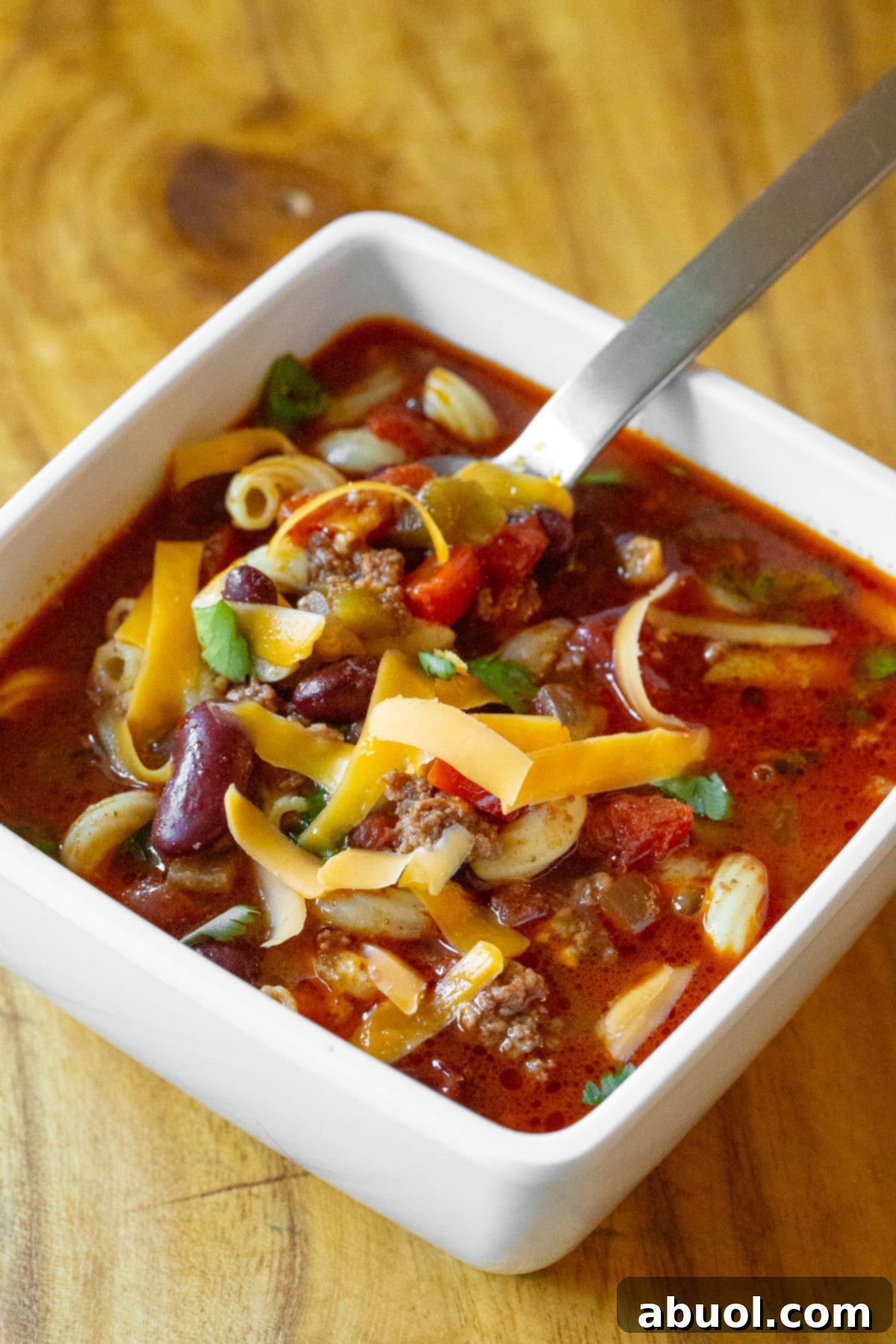 A top-down view of a single serving of slow cooker chili mac and cheese in a rustic bowl, with a spoon ready for digging in, highlighting the rich, comforting texture.