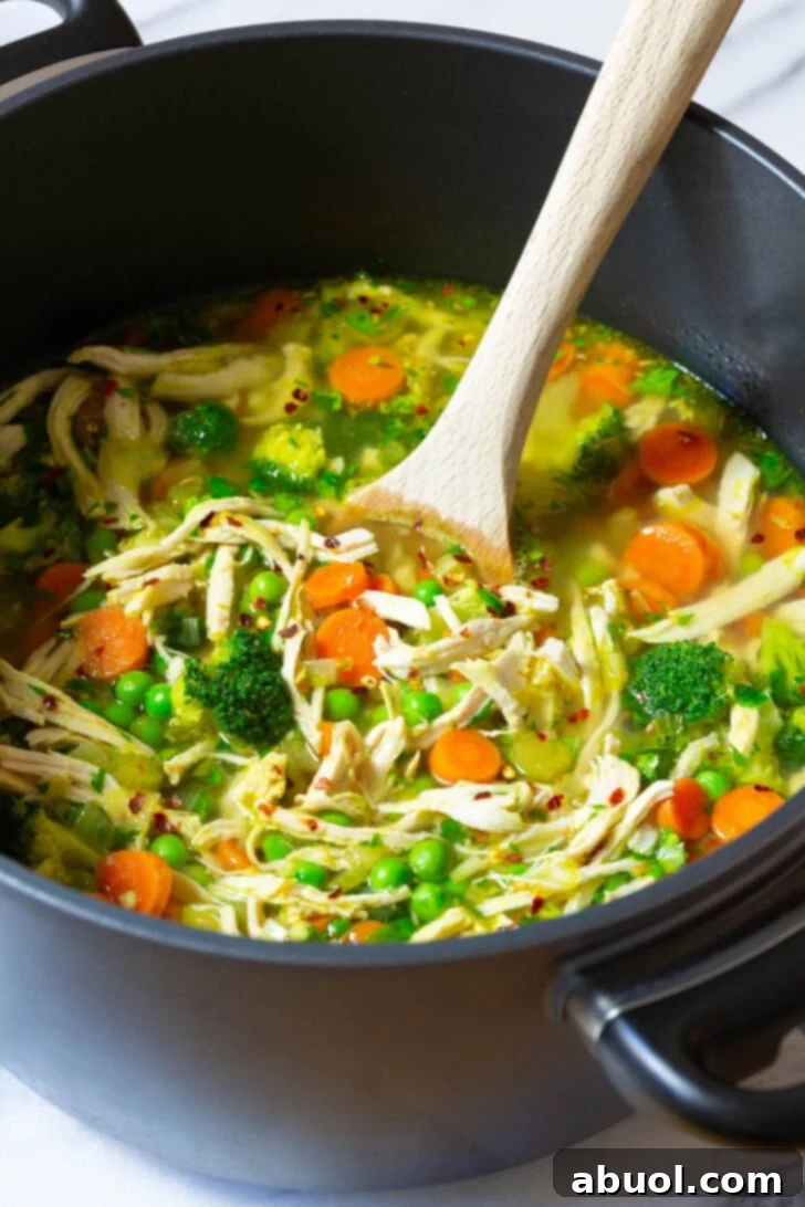 A large pot of simmering chicken detox soup, being stirred gently with a wooden spoon, showcasing its rich texture and vibrant vegetables.