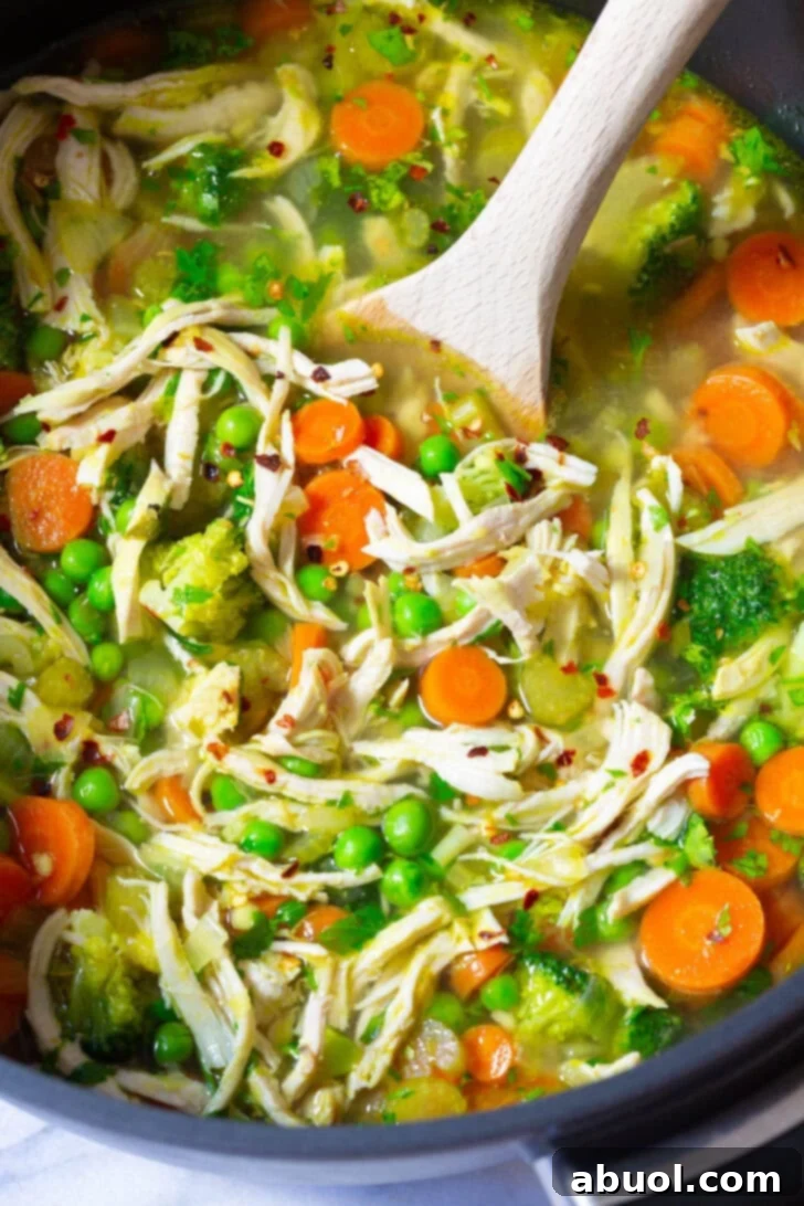 A close-up view of the chicken detox vegetable soup simmering in a pot, with a wooden spoon stirring the rich, flavorful broth.