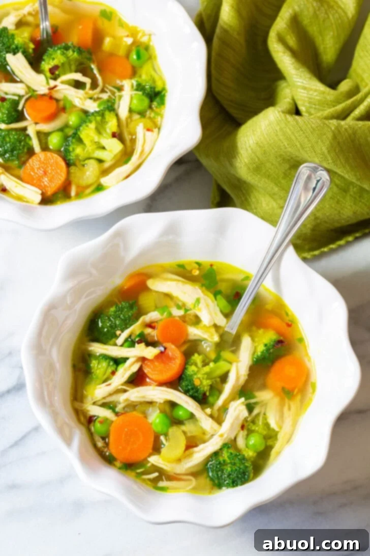 Two pristine white bowls brimming with comforting chicken detox soup, garnished with fresh green parsley, inviting a healthy meal.