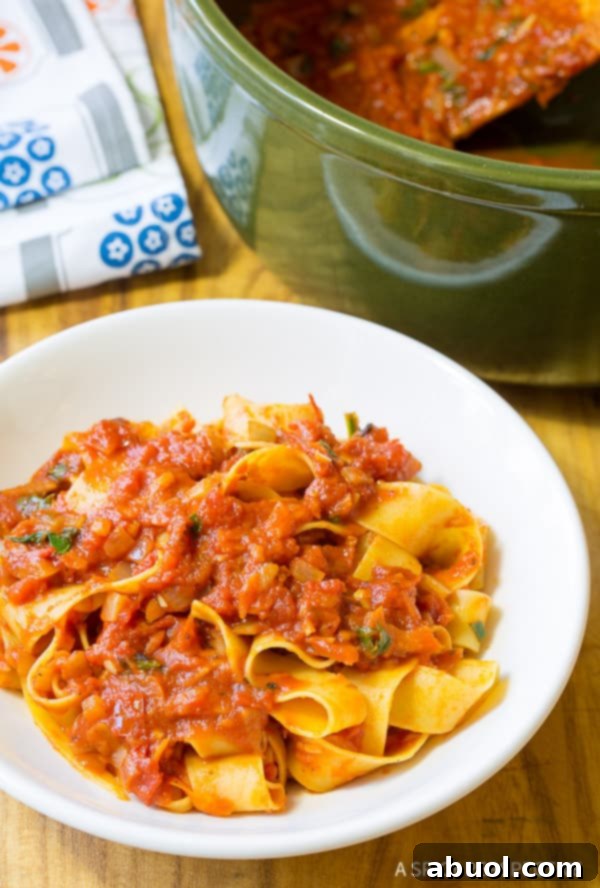 A beautifully plated dish of papardelle pasta generously topped with rich, fresh homemade tomato sauce and garnished with basil.