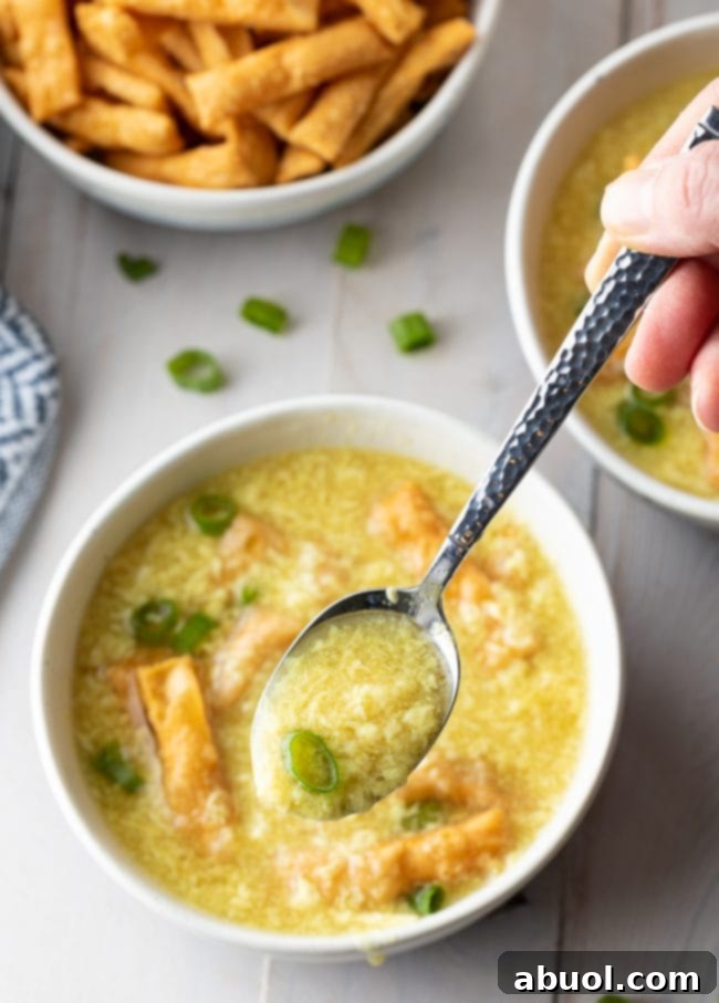 A single bowl of golden egg drop soup, topped with fresh green onions and crispy noodles, showcasing its inviting texture and rich color.