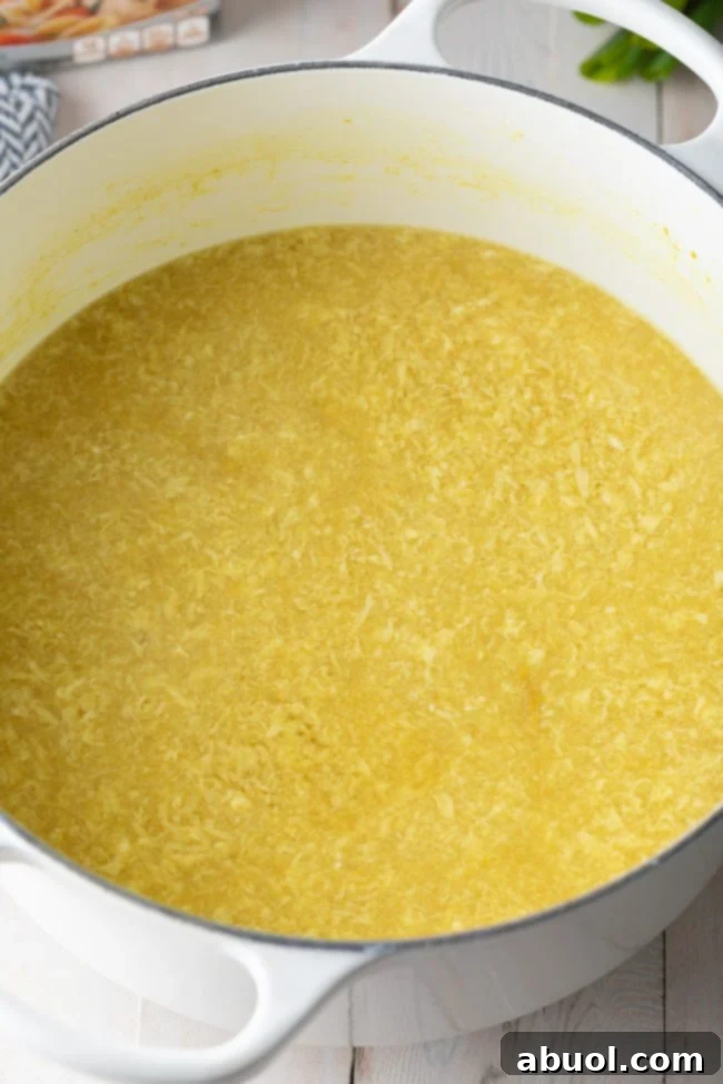 A large pot filled with beautifully textured egg drop soup, featuring numerous delicate egg ribbons floating in the golden broth.