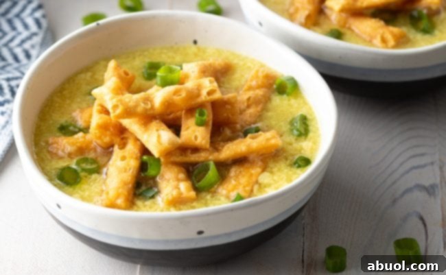 A close-up of a bowl of homemade egg drop soup, generously topped with vibrant green onions and golden crispy noodles.