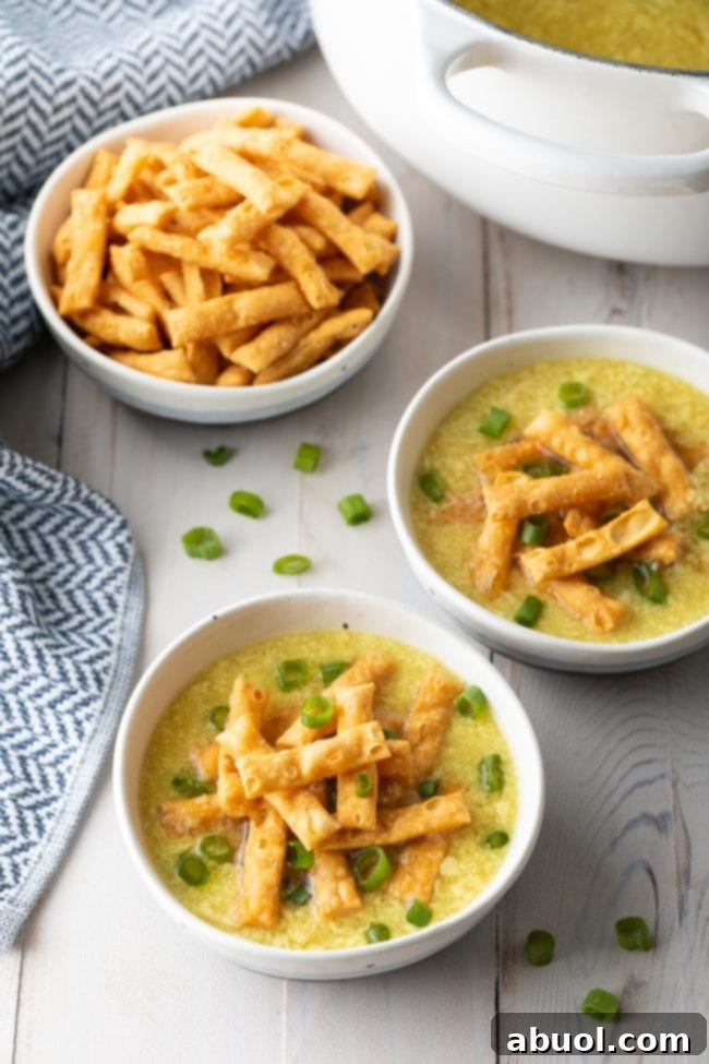 Two beautiful bowls of egg drop soup, artfully garnished with crispy noodles and finely sliced green onions, inviting you to take a spoonful.