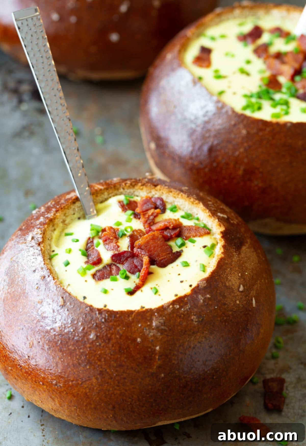 A steaming bowl of Best Irish Beer Cheese Soup in a bread bowl, garnished with crispy bacon and fresh chives, ready to be enjoyed.