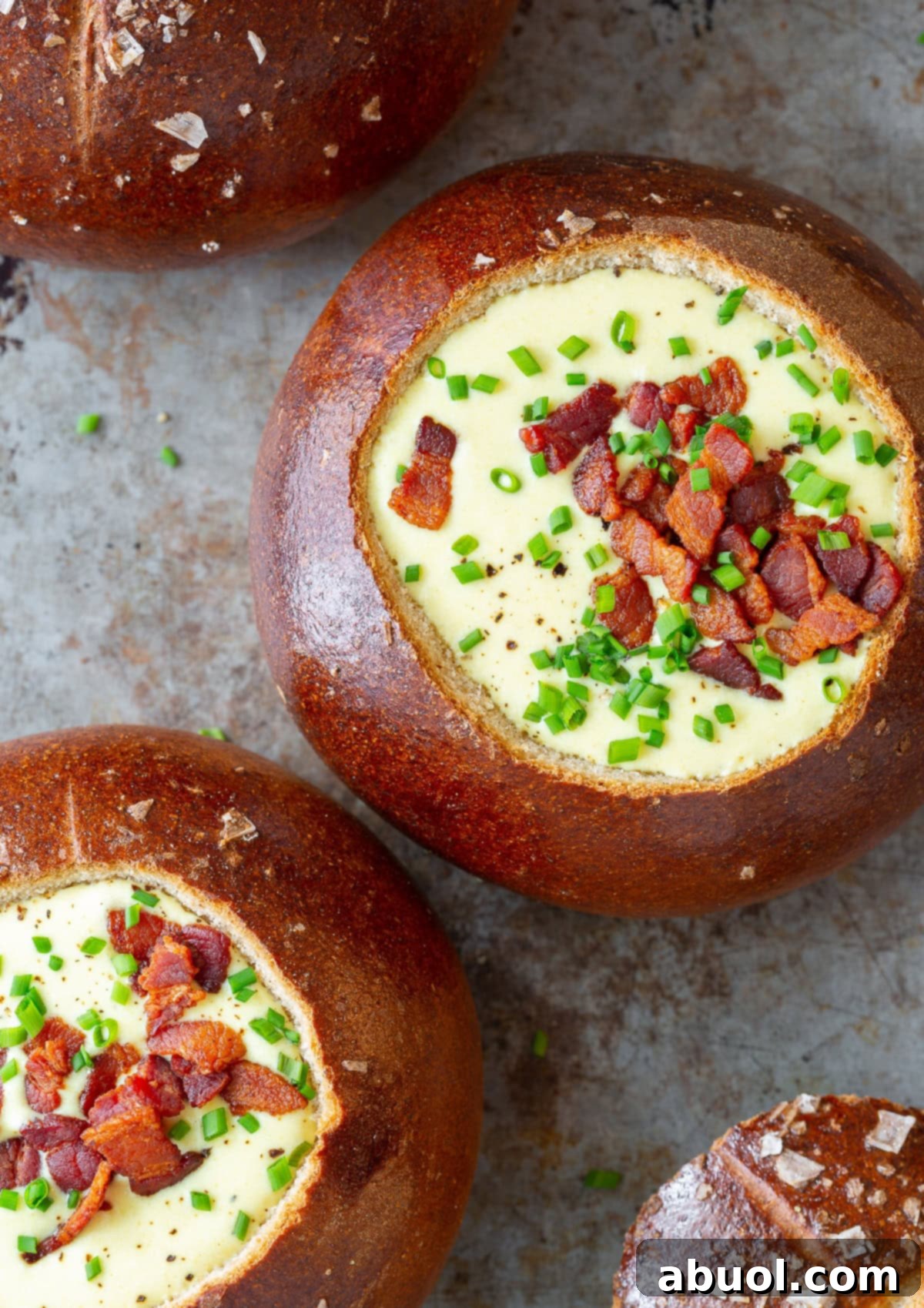 Several golden bread bowls, hollowed out and filled with creamy Irish Beer Cheese Soup, garnished with fresh herbs, showcasing a comforting and visually appealing presentation.