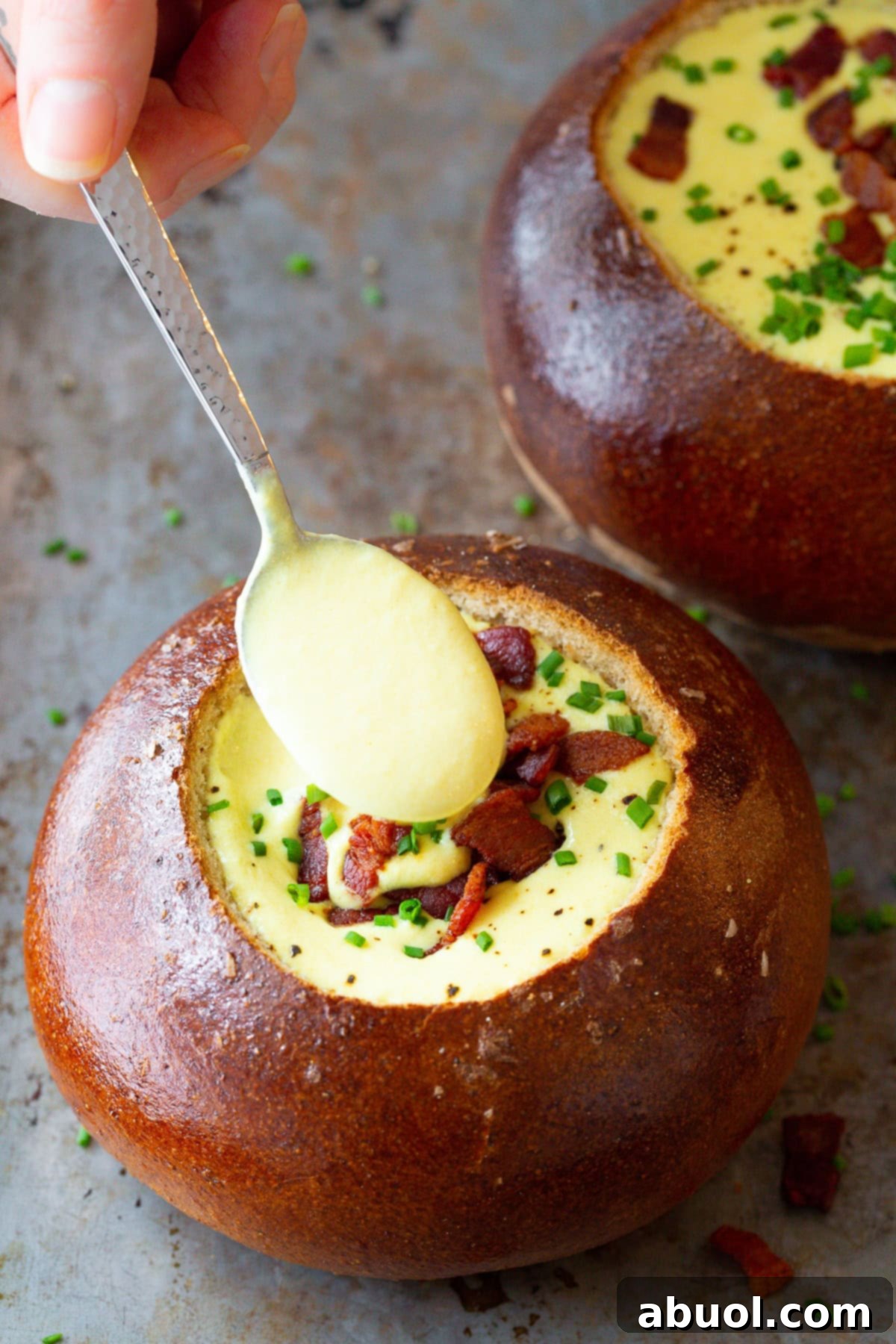A large serving spoon lifts a generous scoop of creamy Irish Beer Cheese Soup above a rustic bread bowl, showing the soup's rich texture and golden color.