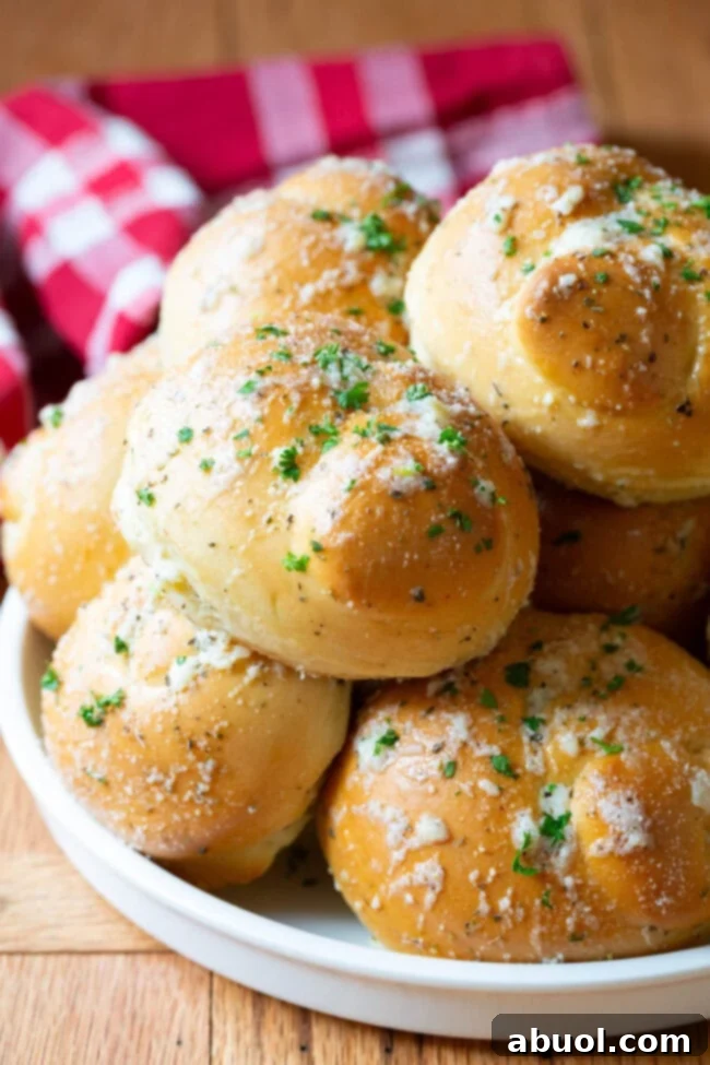 Garlic knots piled on top of each other on a white plate, showcasing their golden-brown crust and glistening garlic butter.