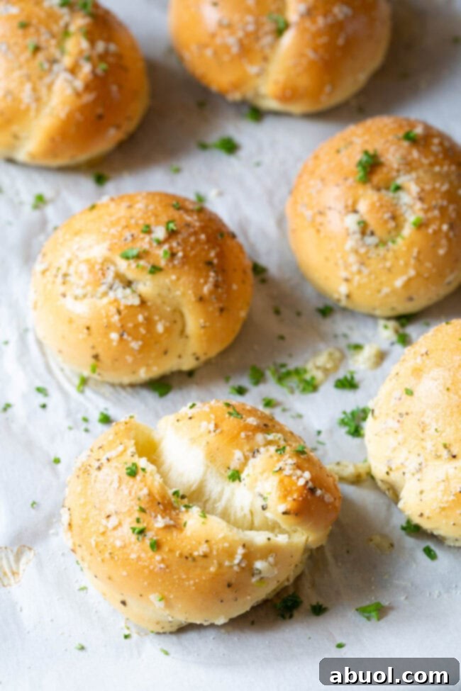 A single garlic knot ripped open to showcase its fluffy, tender interior, with more knots visible in the background on a baking sheet.