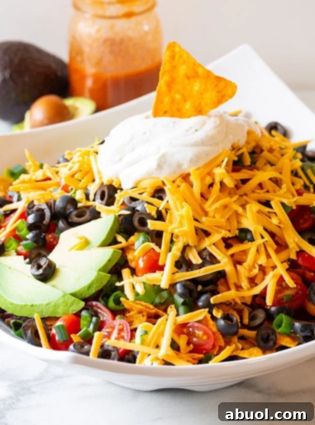 A top-down view of a fully loaded Doritos taco salad with generous dollops of ranch sour cream arranged around the perimeter, showcasing all the fresh, colorful toppings.