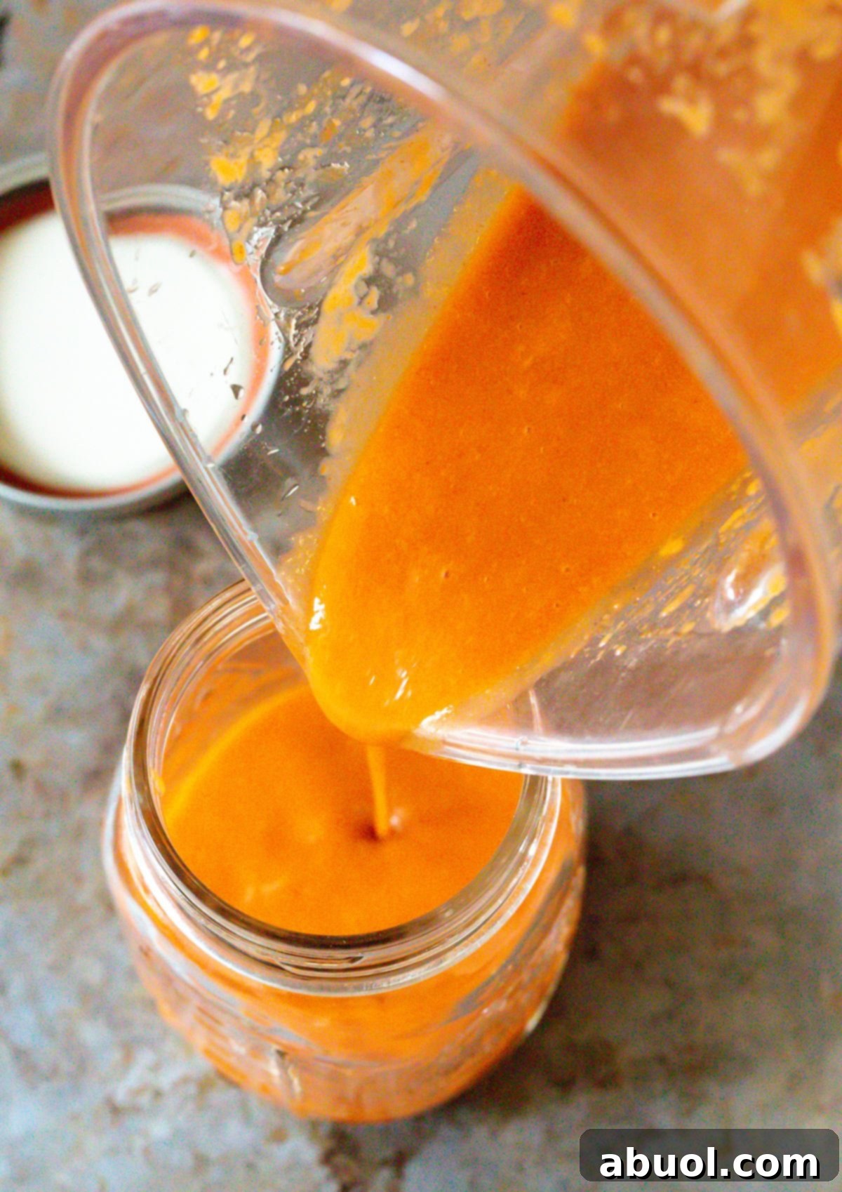 Pouring freshly made Catalina salad dressing from a blender into several mason jars for storage.