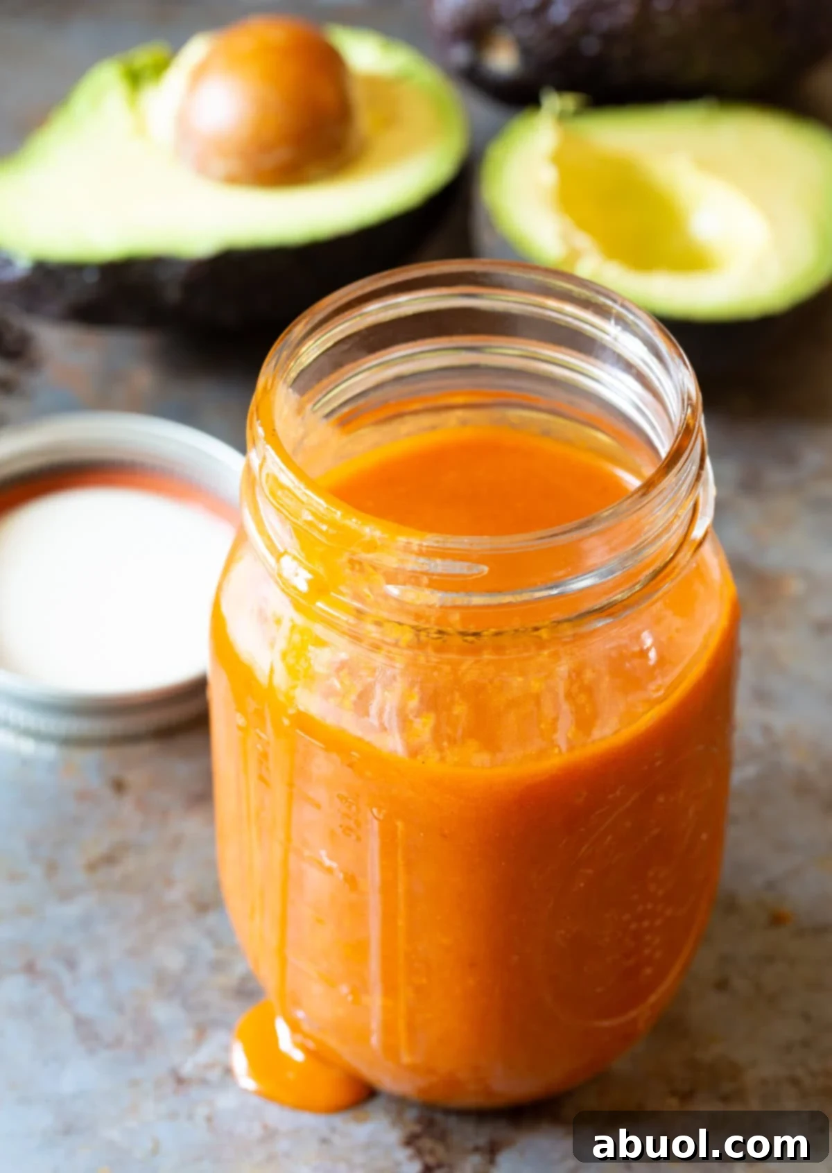 A mason jar filled with vibrant Catalina dressing, with fresh avocado halves and a spoon in the soft-focus background, ready for serving.