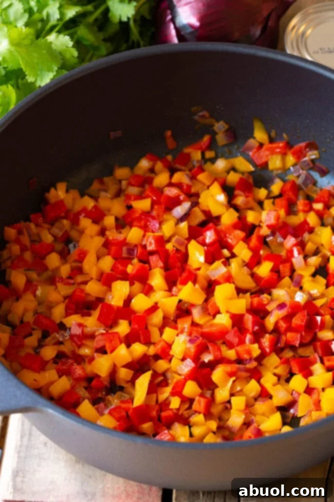 Diced bell peppers and onions being sautéed in a hot pan with butter.
