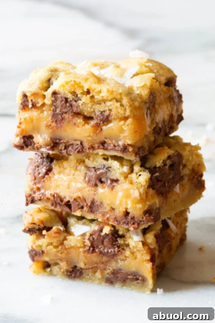Stack of four gooey salted caramel chocolate chip cookie bars with melted caramel showing.