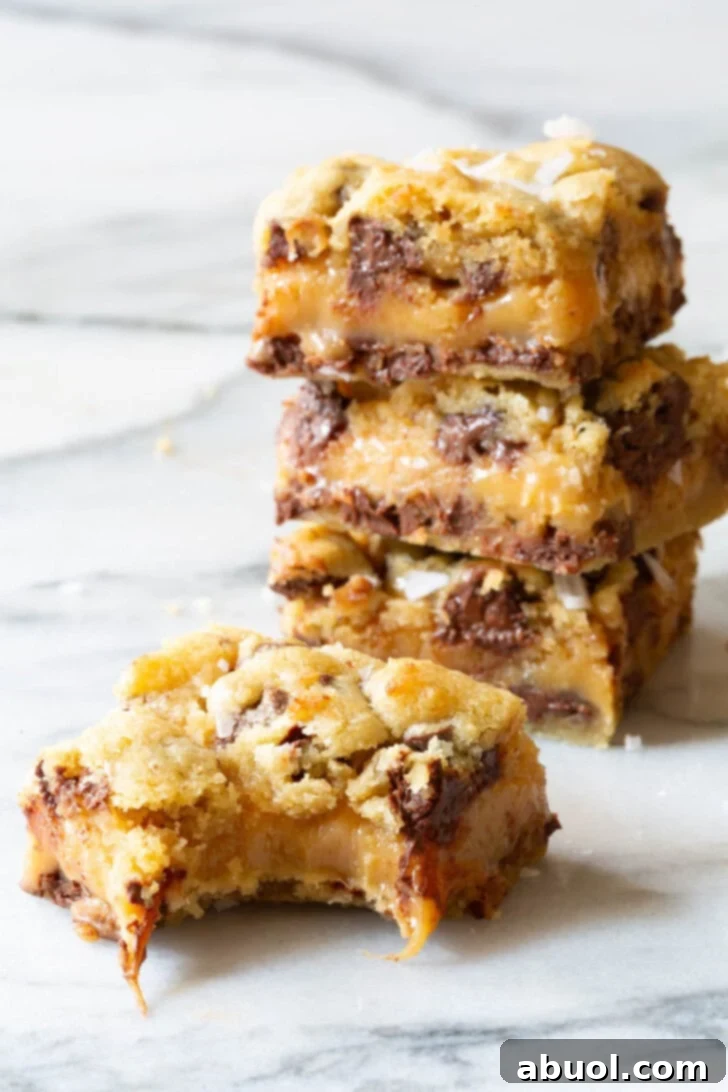 Stack of cookie bars with one in front with a bite taken from it, revealing the gooey caramel center.