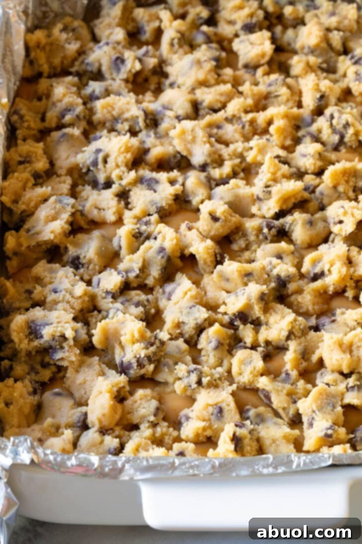Cookie dough pieces dropped on top of caramel in a baking dish lined with foil, ready for baking.