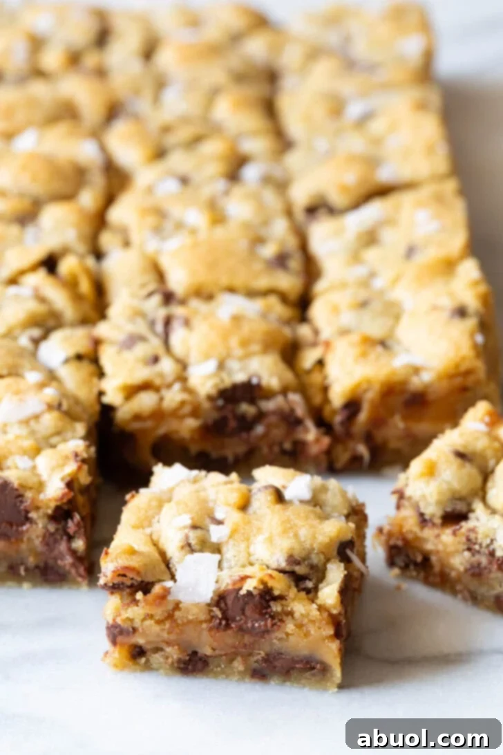 Close-up of a single salted caramel chocolate chip cookie bar with more bars blurred in the background.