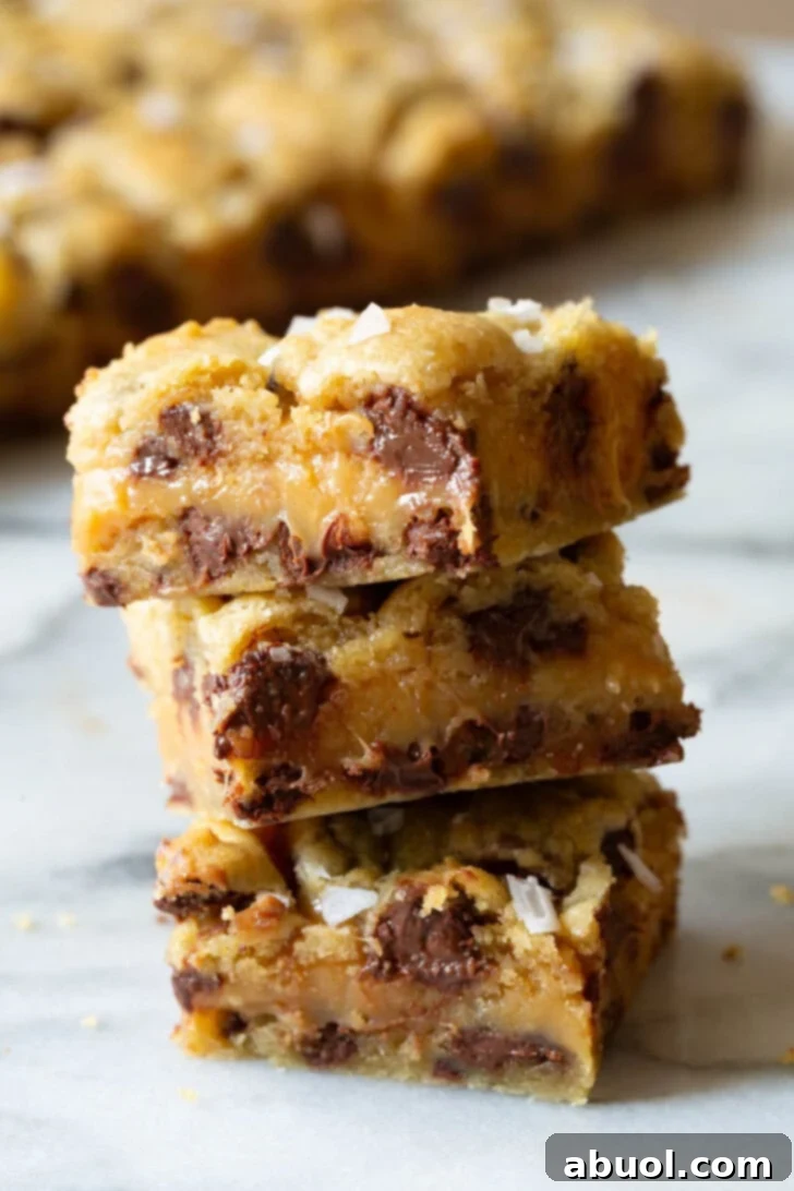 Three salted caramel chocolate chip cookie bars stacked on top of each other, showcasing their layers.