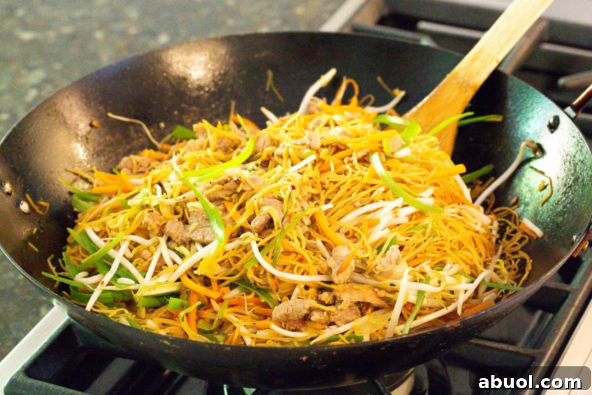Classic Cantonese Pork Lo Mein 7 Fresh egg noodles and vegetables being stir-fried in a large wok for Lo Mein.