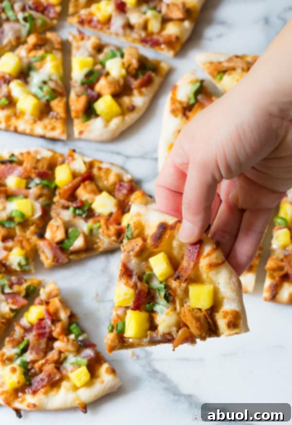 A close-up shot of a hand lifting a perfectly cooked slice of Chicken Teriyaki Pizza, showcasing its appealing golden crust and generous toppings.