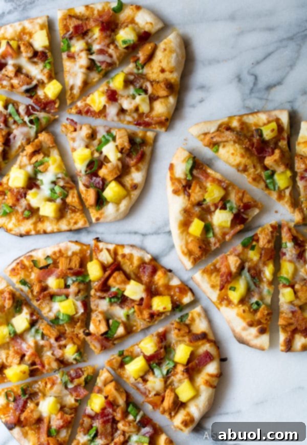 An inviting overhead shot of delicious Chicken Teriyaki Pizza slices artfully arranged on a white backdrop, garnished with vibrant fresh pineapple pieces.