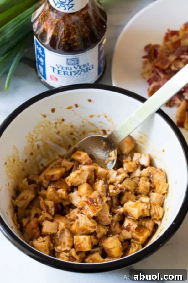 Chopped, grilled chicken being generously marinated in a rich teriyaki sauce within a bowl, soaking up all the delicious flavors.