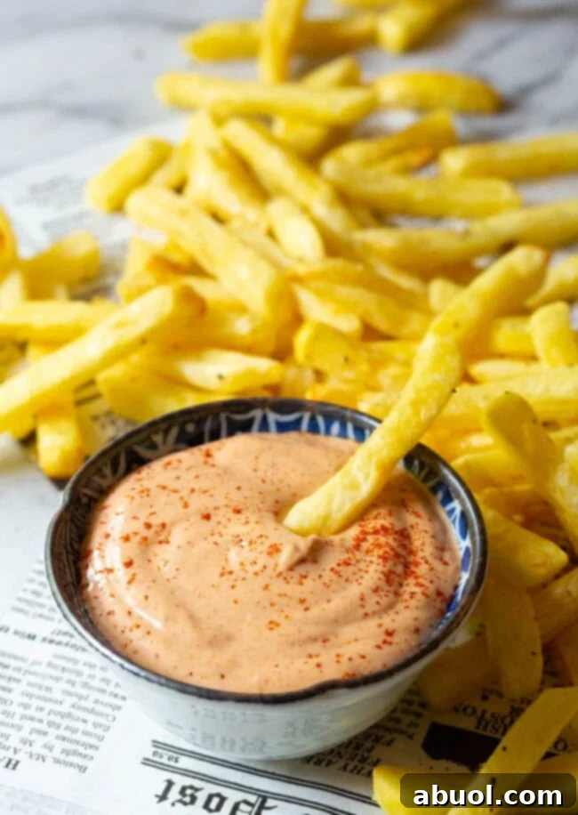 Fries next to a small bowl of southern comeback sauce with one fry being dipped in the sauce. 
