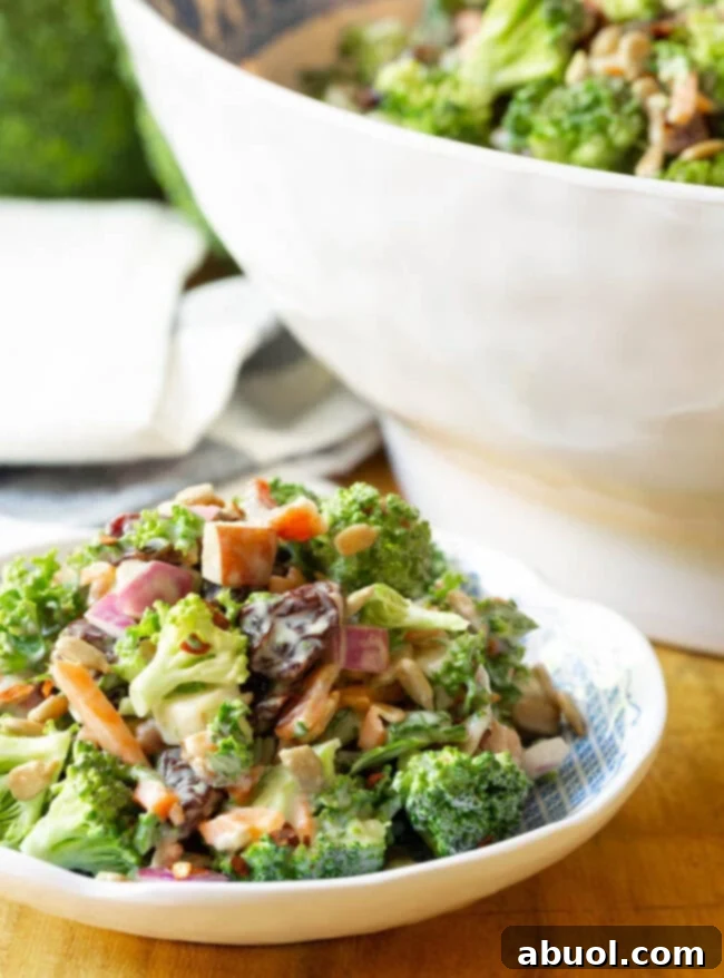 A small plate of Broccoli Bacon Salad with a large bowl of the salad in the soft-focus background, highlighting the fresh ingredients.