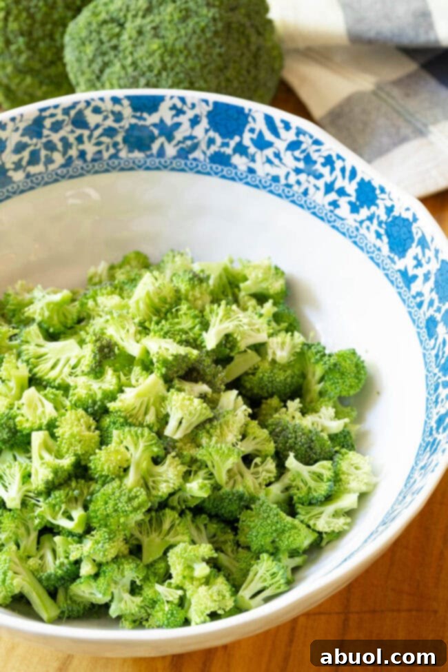 Freshly chopped broccoli florets in a large white bowl, ready for salad preparation.