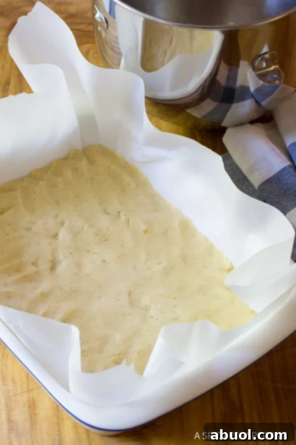 Soft cookie dough perfectly pressed into the bottom of a parchment-lined baking dish, forming an even base for the blueberry bars.