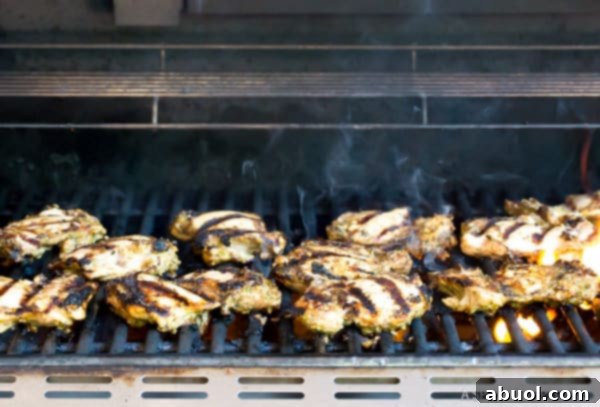 Jerk chicken thighs grilling on an outdoor barbecue, showing a slight char and smoky texture.