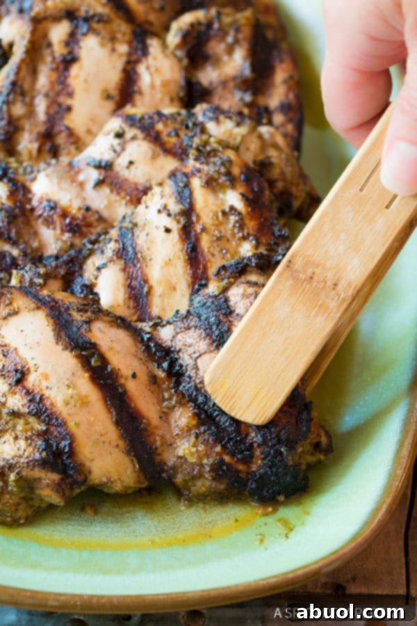 Grilled jerk chicken thighs being lifted off the grill with tongs, ready to be served.