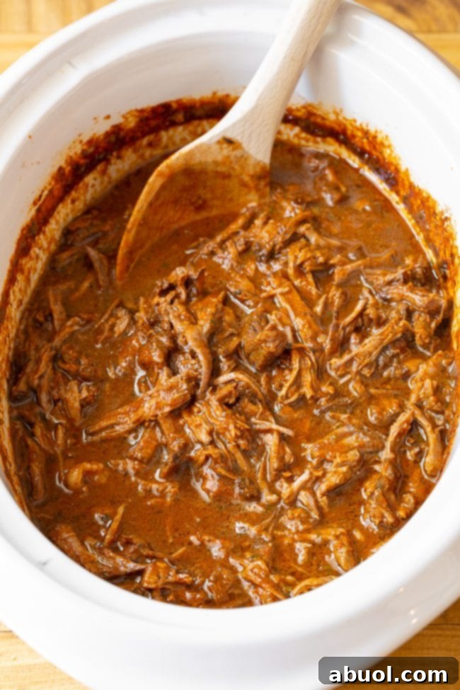 Rich and spicy shredded beef simmering to perfection in a slow cooker, releasing tantalizing aromas.
