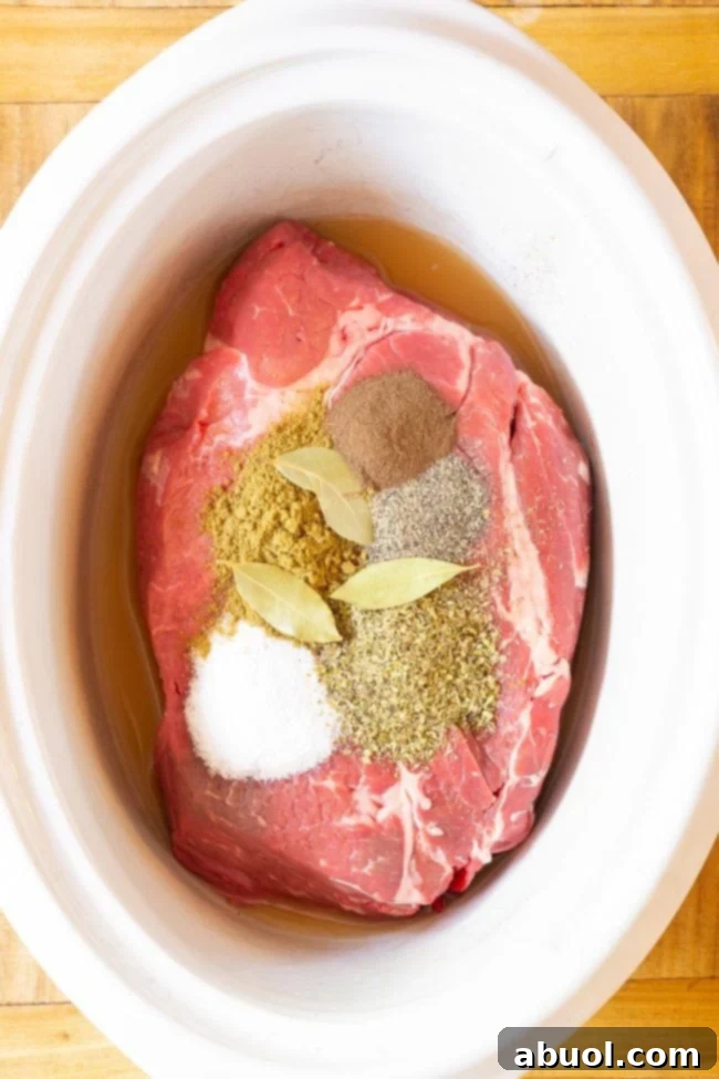 A large, raw beef chuck roast resting at the bottom of a white slow cooker, ready for seasoning and sauce.