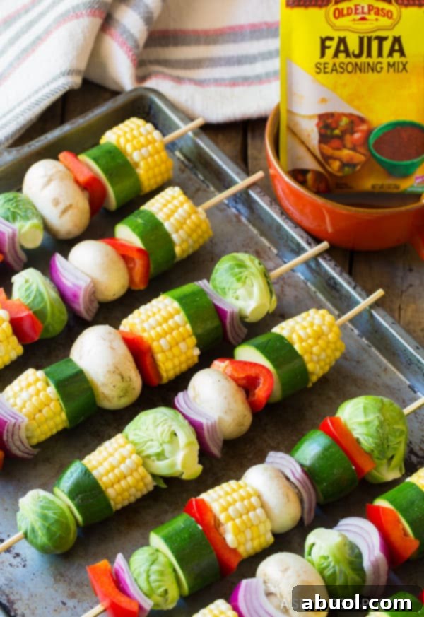 Hand threading a colorful assortment of vegetables including corn, zucchini, peppers, and onions onto a skewer, ready for grilling.