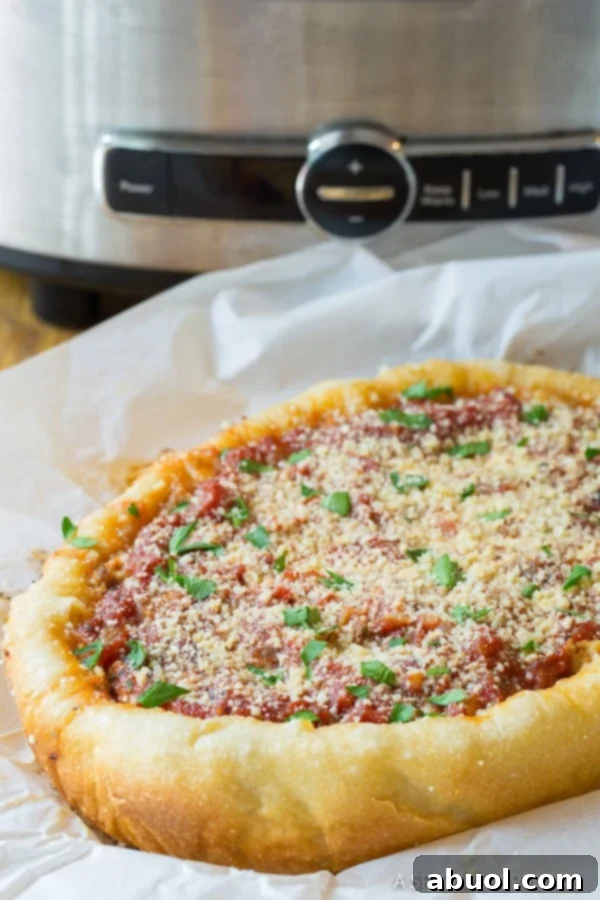 A side profile view of a deeply layered and perfectly golden slow cooker pizza, highlighting its thick crust and rich fillings, with the slow cooker blurred in the background.