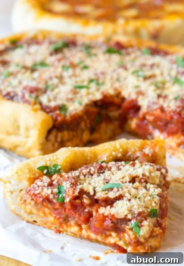 A perfectly cooked slice of slow cooker deep dish pizza, rich with melted cheese and savory sausage, resting on parchment paper with the rest of the pizza in the background.