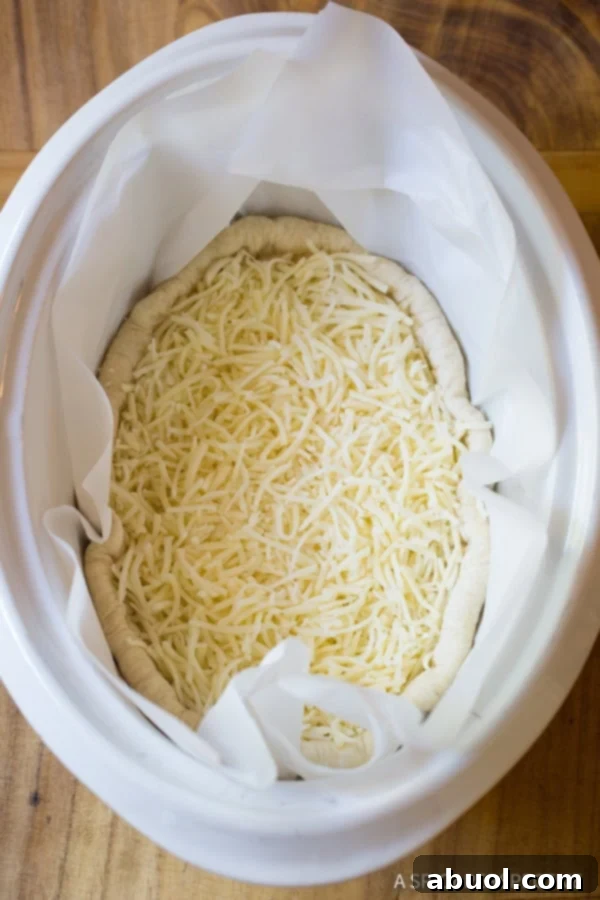 A top down view of the slow cooker deep dish pizza crust, now generously covered with a layer of shredded Italian cheese, extending up the sides of the dough.
