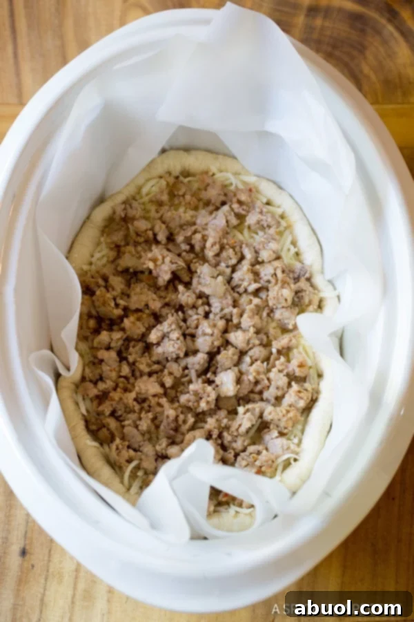 A top down view of the slow cooker deep dish pizza base, now layered with cooked, crumbled Italian sausage over the cheese.